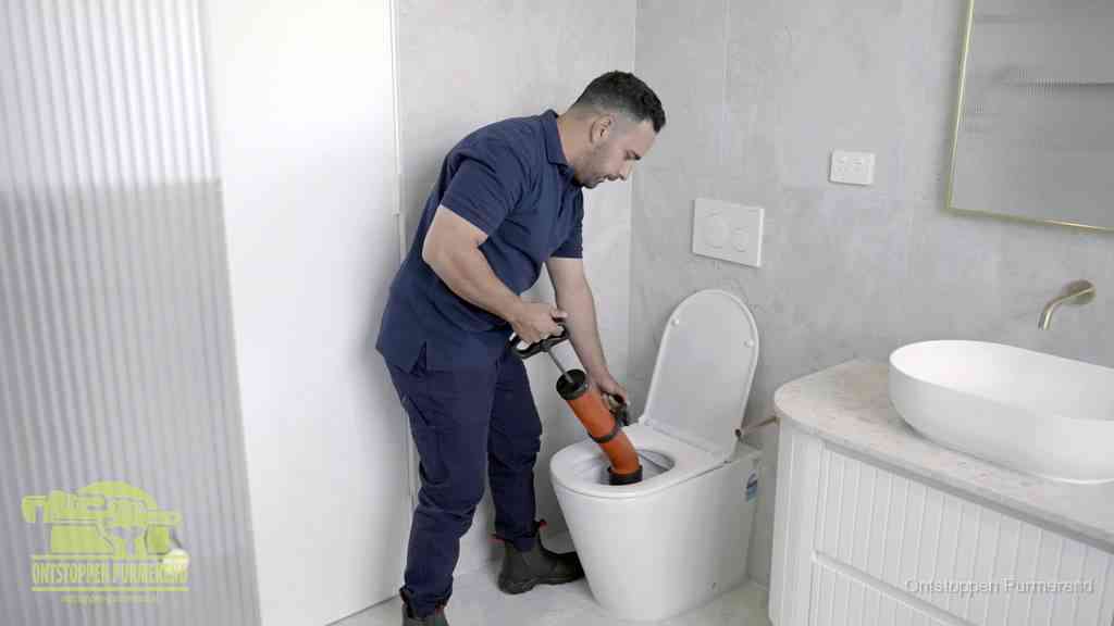 Een monteur buigt over een wandcloset en duwt met de hand een persluchtontstopper in de toiletpot om de verstopping handmatig los te maken in Purmerend