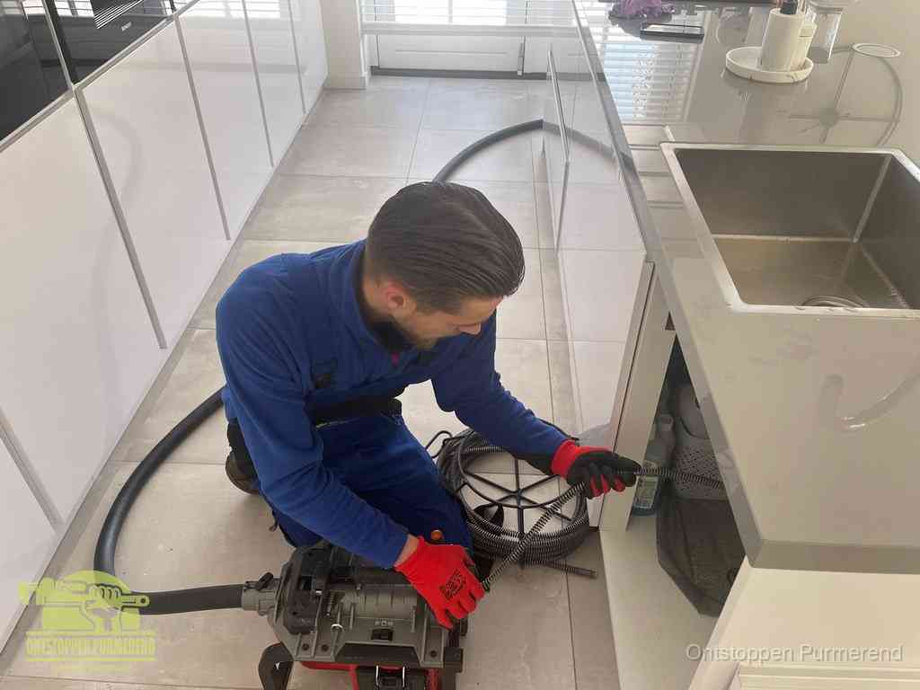 Een monteur ontstopt de keukenafvoer onder de spoelbak met een elektrische veermachine in Purmerend