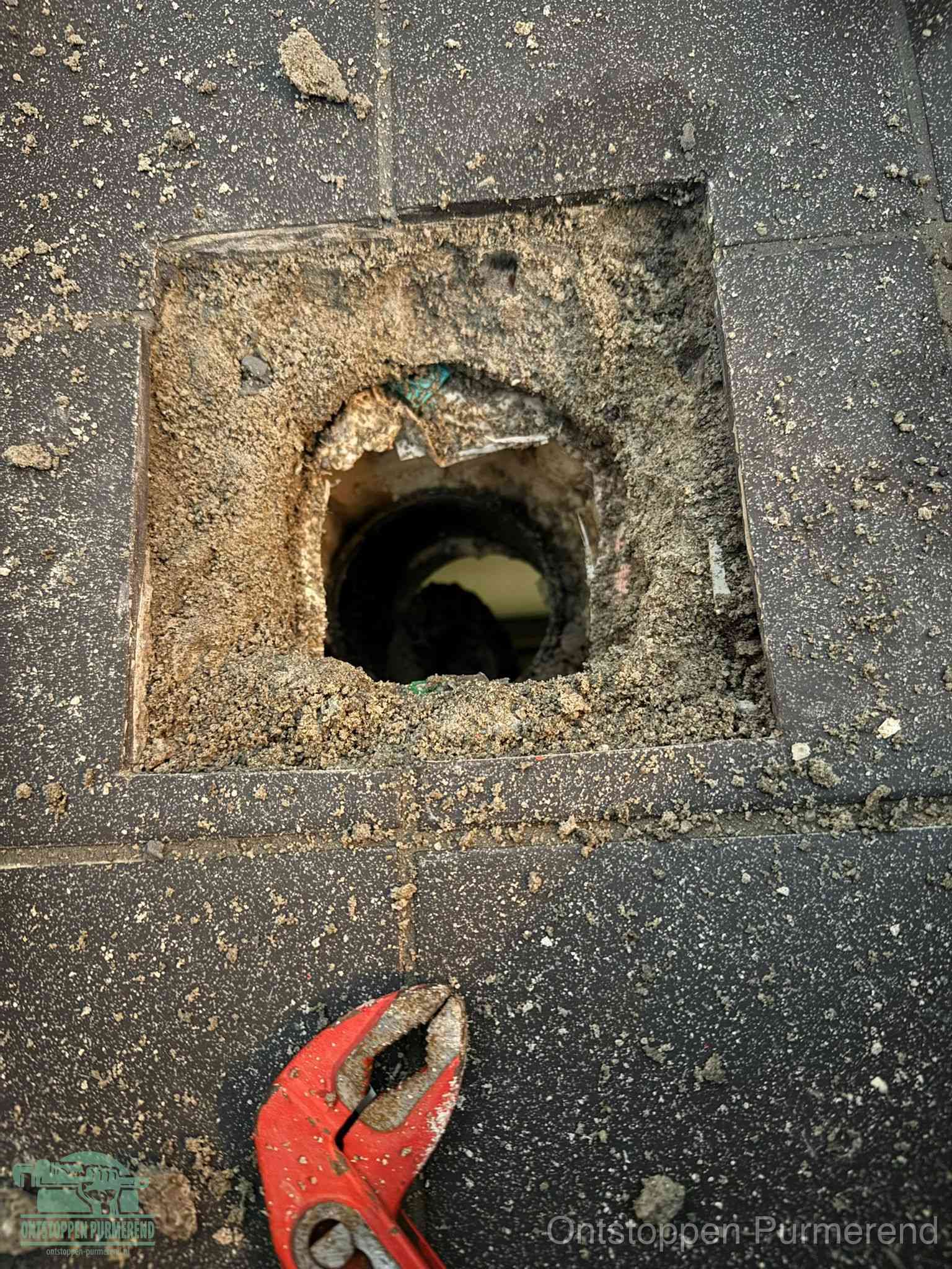 Een geopend rioolputje in een betontegelvloer met losgemaakt rooster en een zichtbare ronde afvoerbuis, het achterhalen waar de afvoerverstopping zit in Purmerend