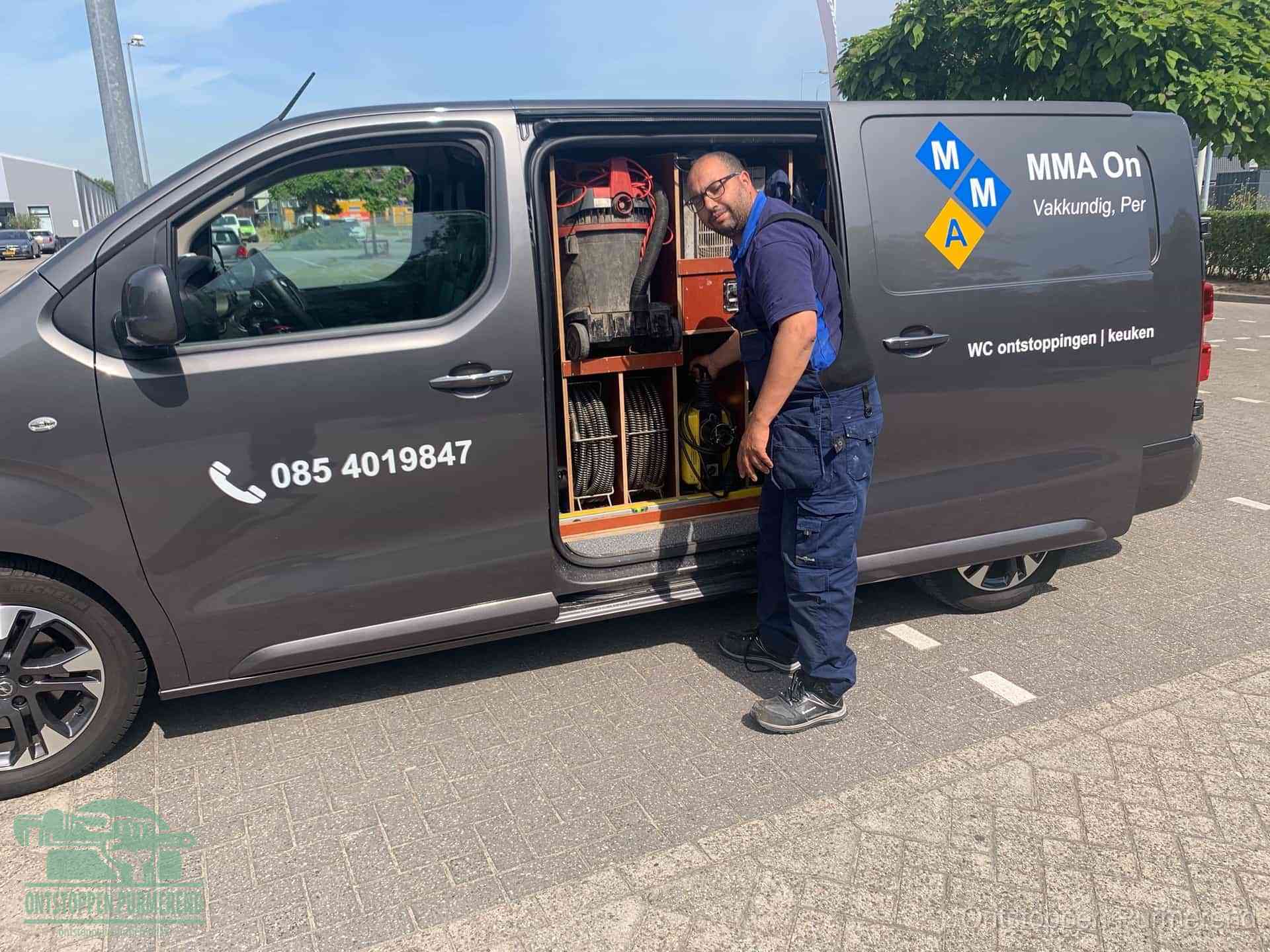 Een monteur bij de open schuifdeur van zijn bedrijfsbus op een parkeerplaats, klaar om de oorzaak van terugkerende afvoerverstoppingen aan te pakken in Purmerend