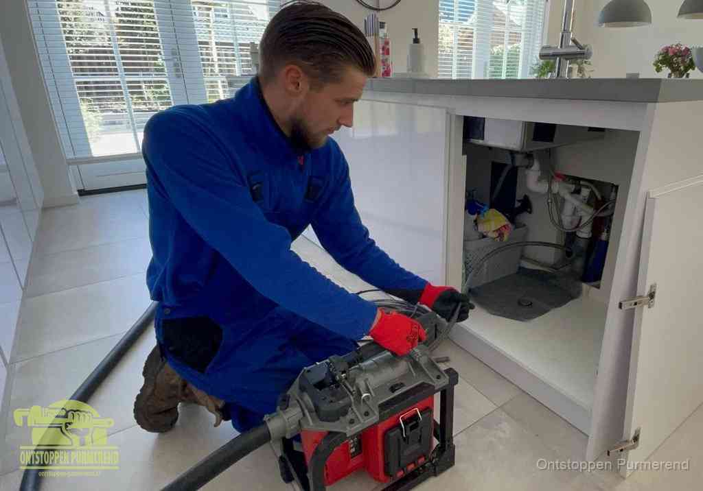 Een monteur voert een professionele elektrische ontstoppingsmachine in de afvoer onder de spoelbak tijdens het gootsteen ontstoppen in Purmerend