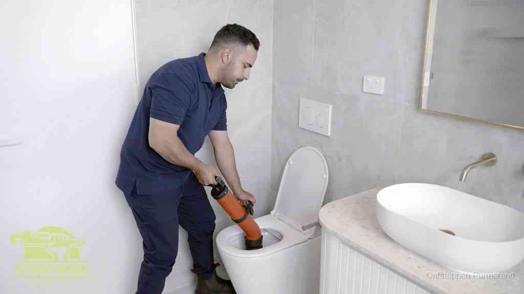 Een man gebruikt een handmatige luchtdruk-ontstopper in een modern betegeld toilet om zelf de wc te ontstoppen in Purmerend